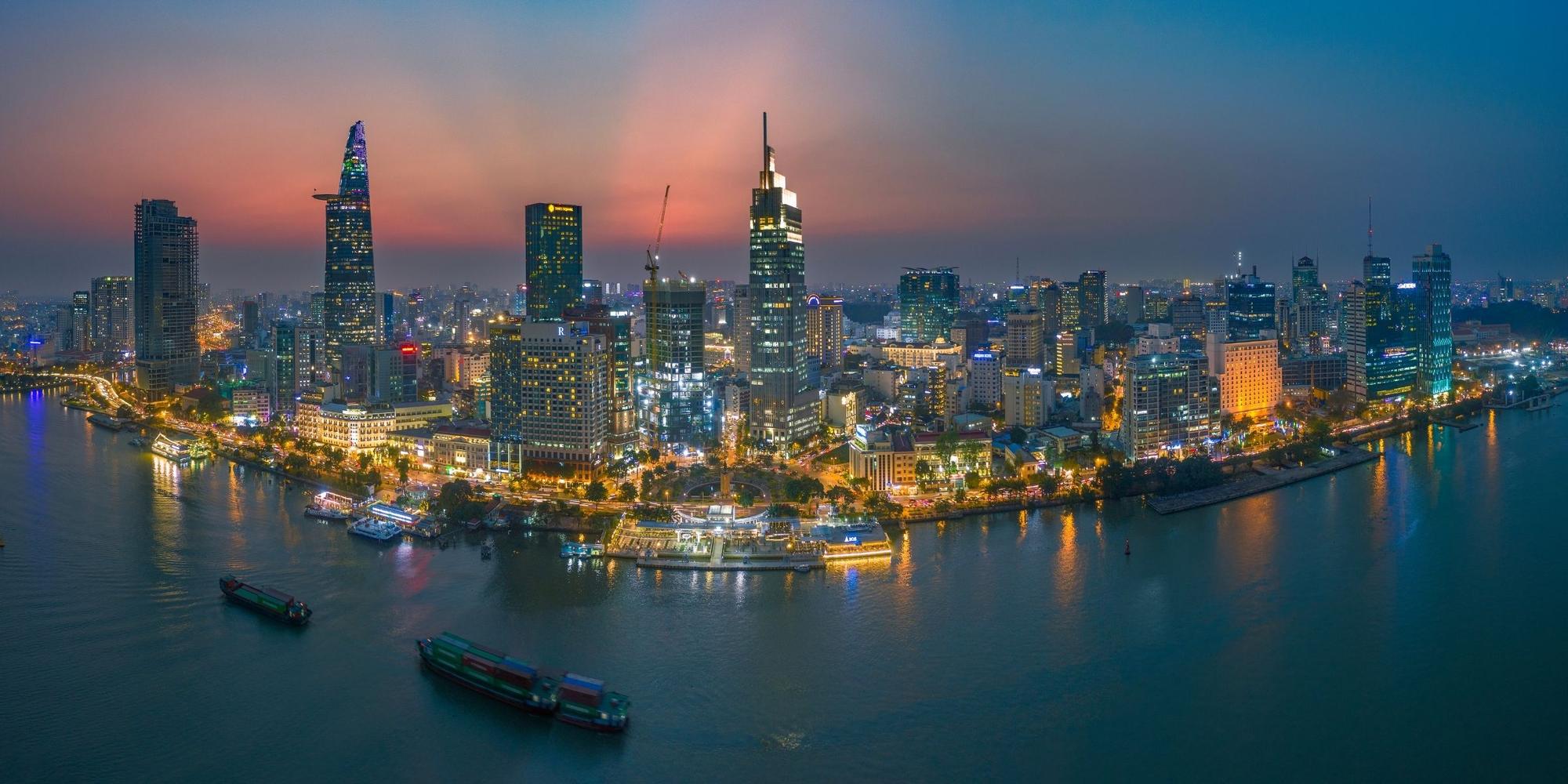 Ho Chi Minh City skyline at night along the Saigon River, with cargo barges on the water